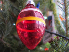 A close-up of a red Christmas bauble, with an orange line round it, hanging on a tree